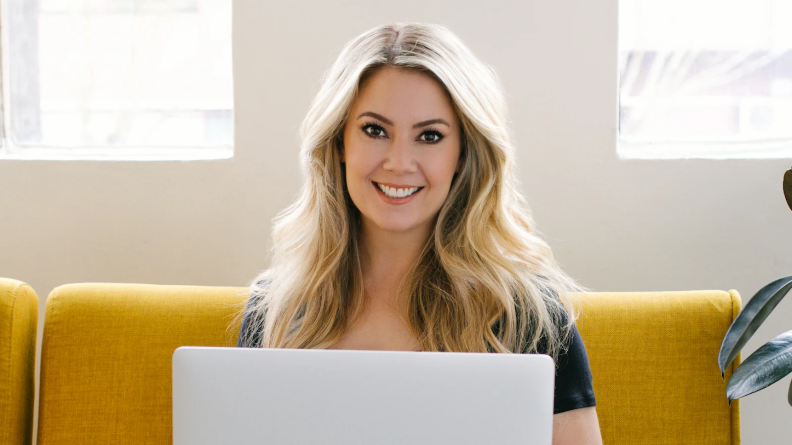 Elizabeth Rider seated on a yellow sofa with a laptop.